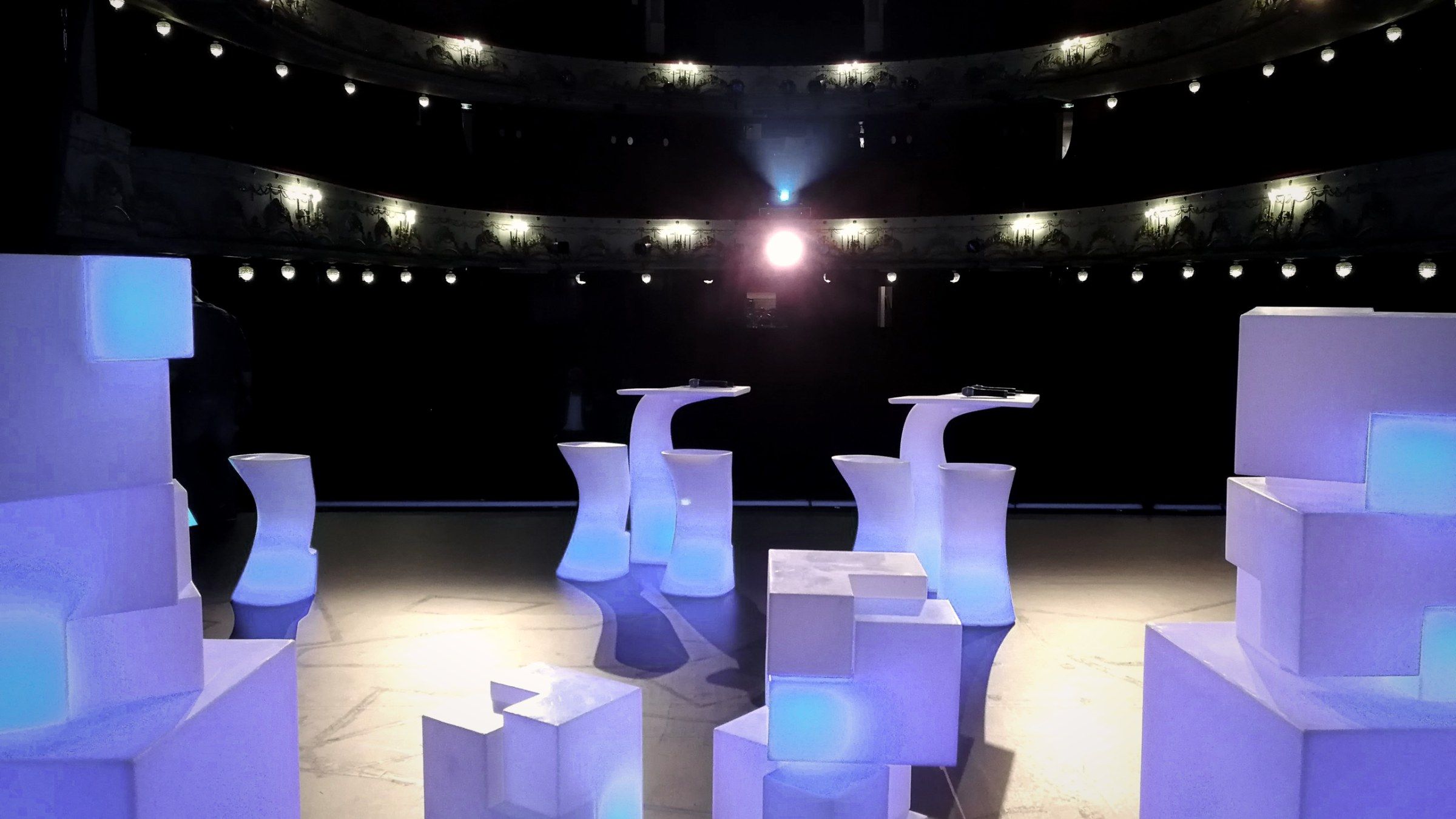 La salle d'un théâtre vue depuis la scène, mange-debout blancs installés sur le plateau.